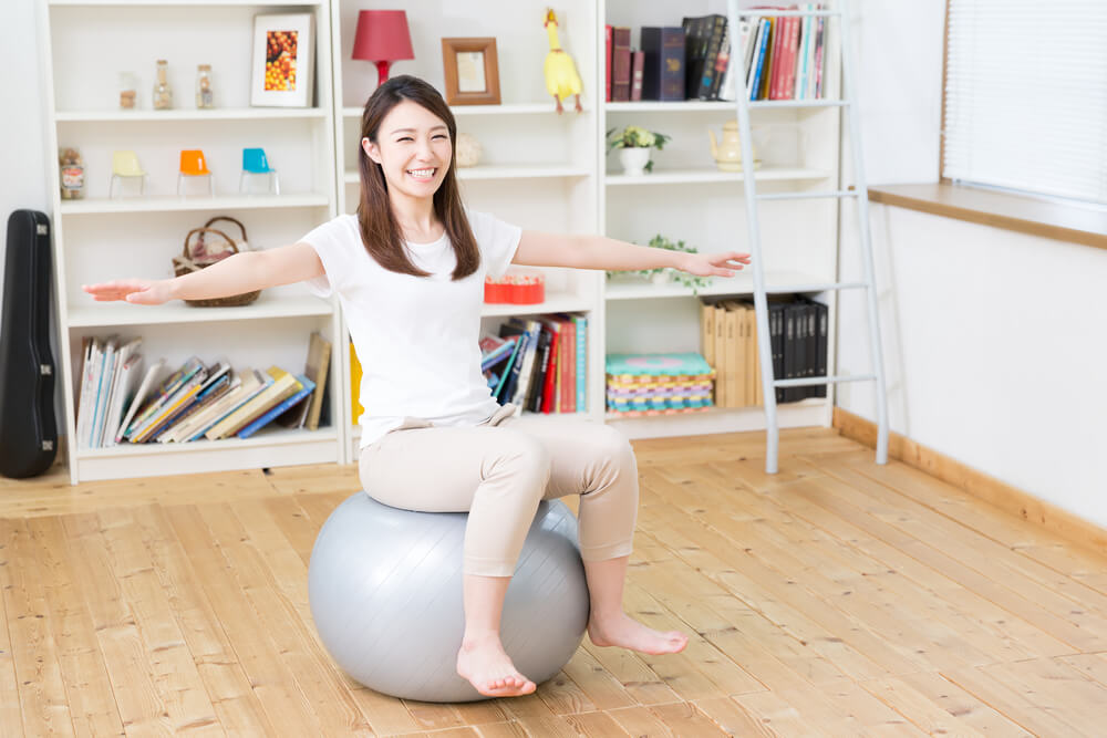 部屋でバランスボールに乗る女性