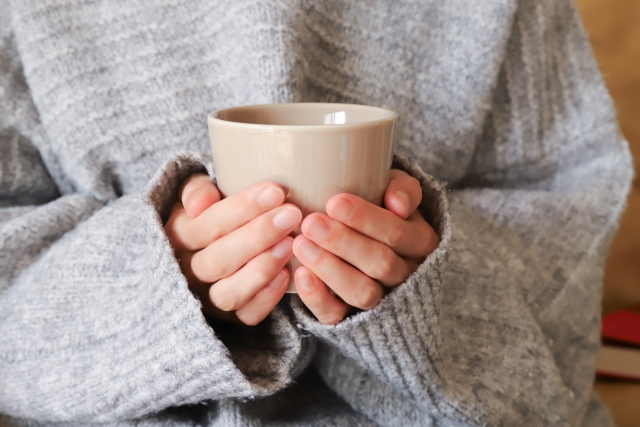 ホットドリンクを持つ女性の手元