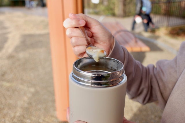 スープジャーに入ったクラムチャウダーを屋公園で食べる男性の手元　別角度