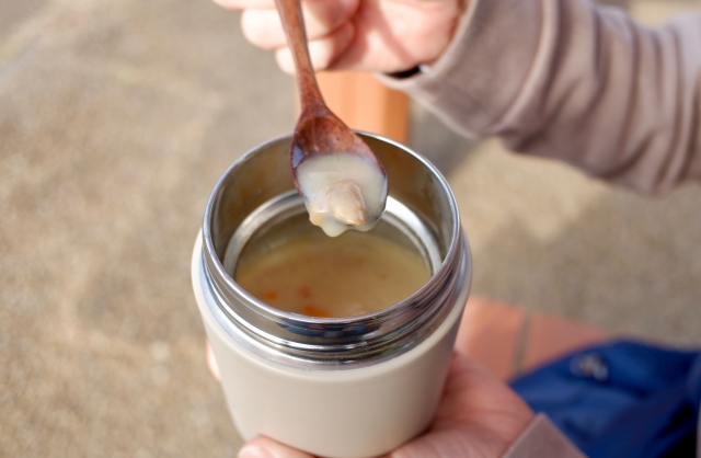 スープジャーに入ったクラムチャウダーを屋外で食べる男性の手元