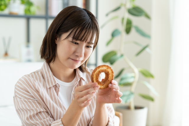 ドーナツを食べるかどうかを、ドーナツを持って悩む女性