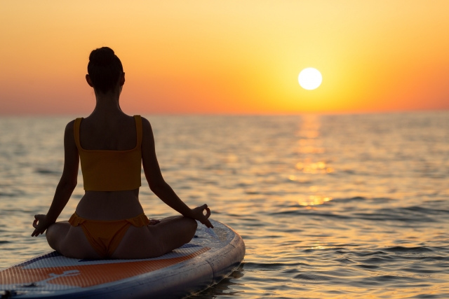 夕日と海を前にヨガをする女性の後ろ姿