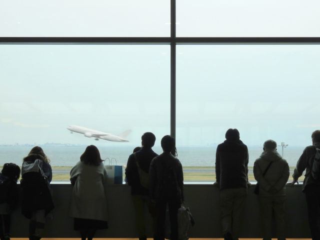 空港の展望デッキにて、離陸する飛行機を見る人々