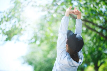 明るい日差しの中で伸びをする運動着の女性