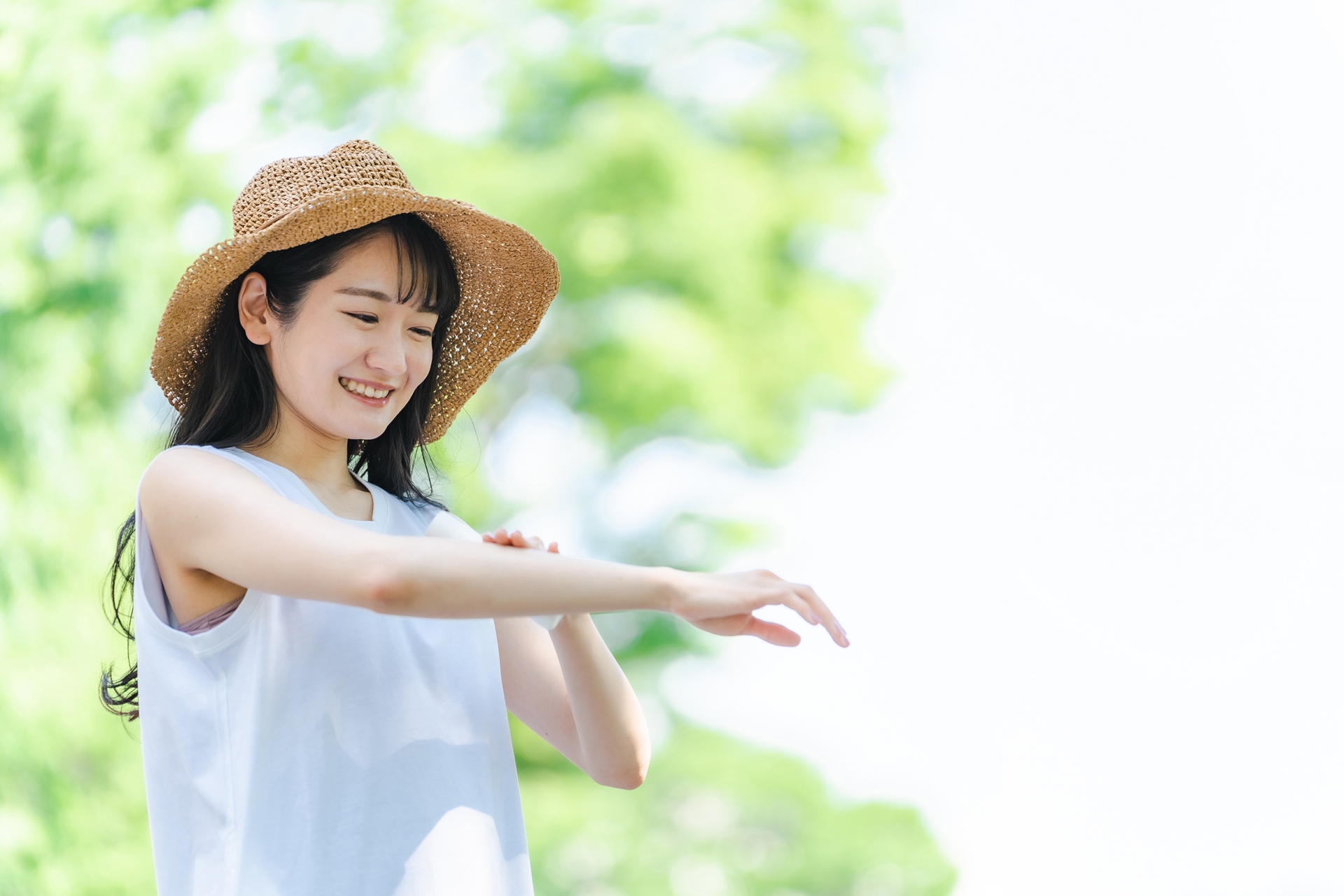 屋外　腕に日焼け止めを塗る麦わら帽子を被った女性