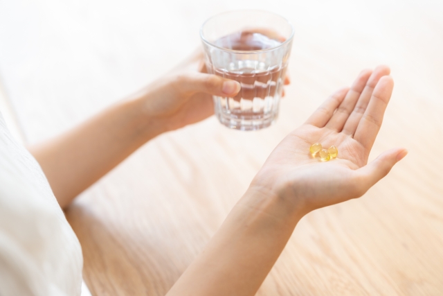 ビタミンのサプリを飲む女性の手元　コップ