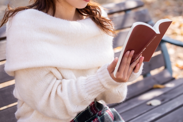 秋 紅葉散る中ベンチで読書する女性