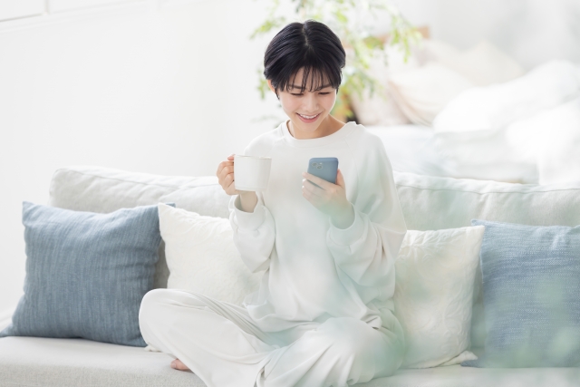 朝のコーヒーを片手にスマホを見るパジャマを着た女性
