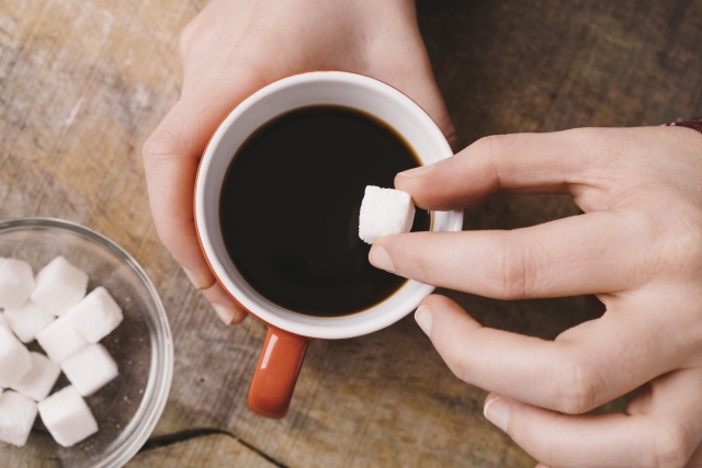 コーヒーの入ったマグに角砂糖を入れる様子