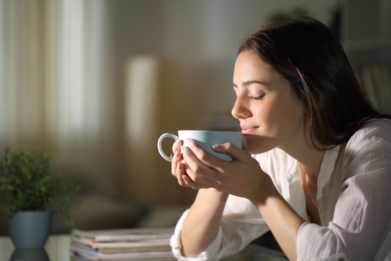 マグカップに入ったコーヒーの香りをかいでリラックスする女性