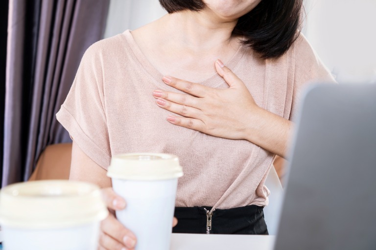 カフェインの過剰摂取　動悸　イメージ　コーヒーを持って仕事をする女性