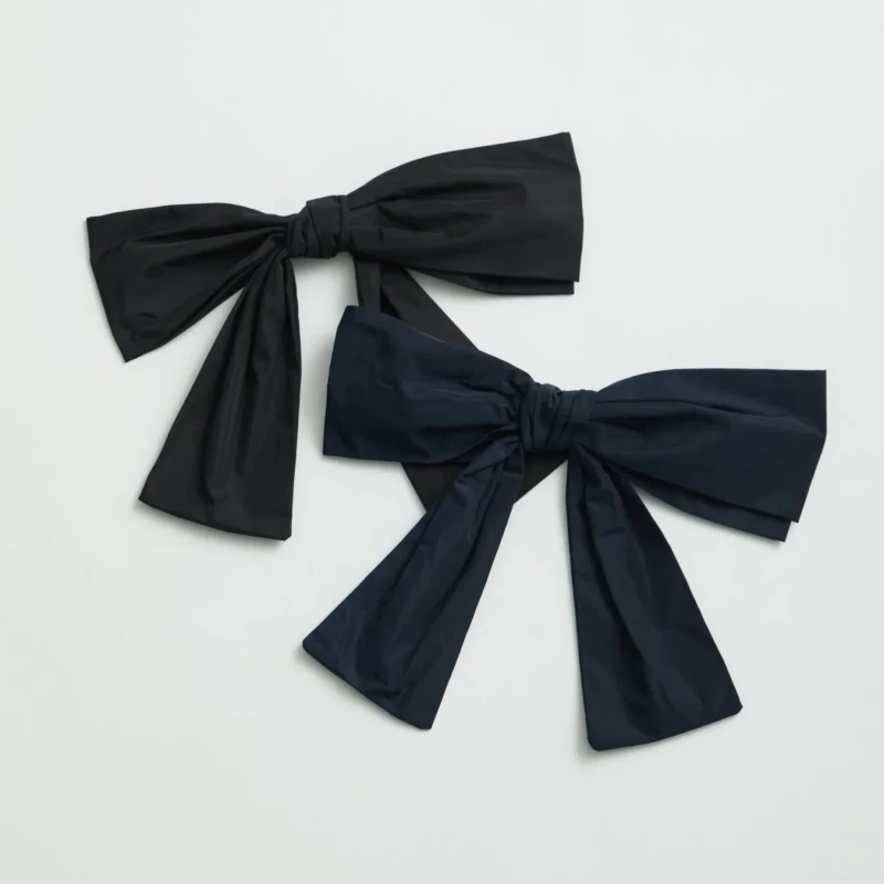 白い背景に2つの大きなリボンが並んで置かれています。1つは黒、もう1つは濃紺です。