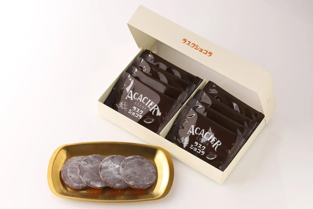チョコレートのお菓子が箱に入っている写真。箱の中には個包装されたチョコレートラスクが入っており、手前には金色の皿に盛られたチョコレートラスクが写っています。