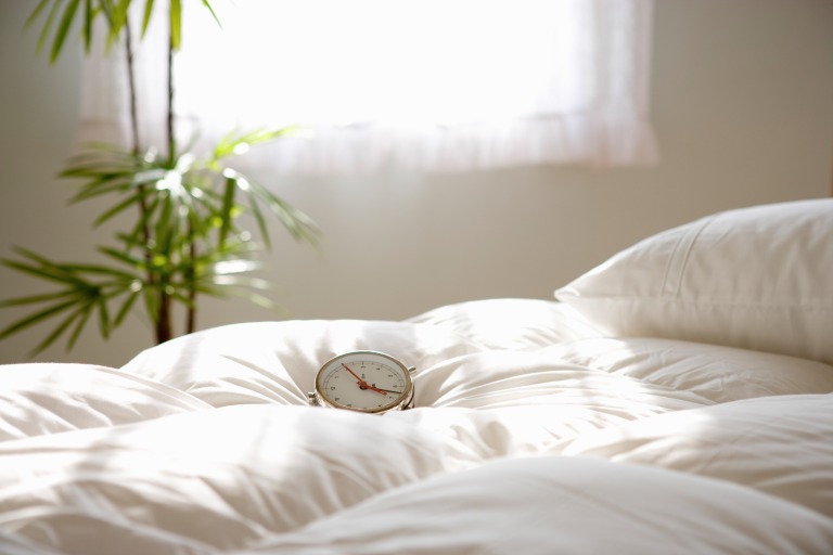 朝日の中のベッドと目覚まし時計　朝起きる