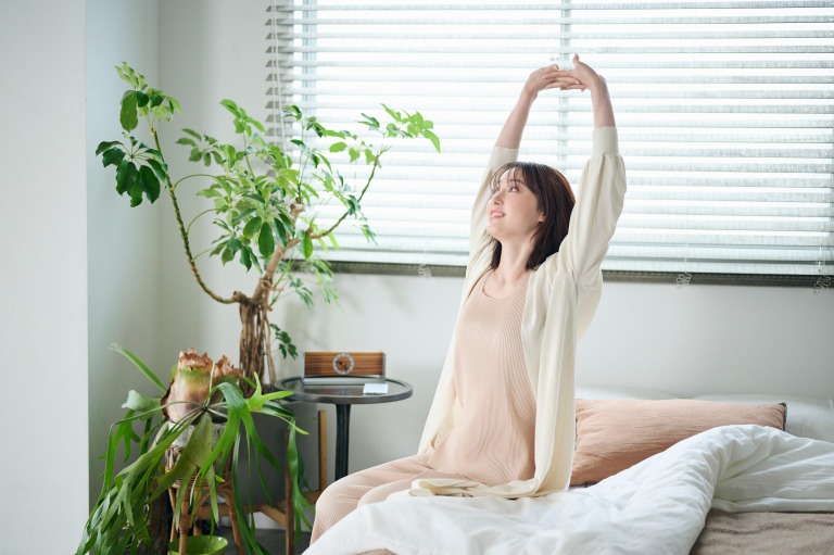 目が覚めてベッドで体を伸ばす20代女性