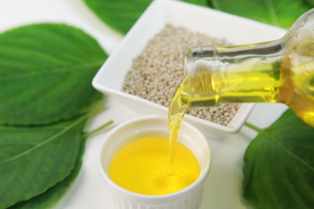 エゴマの実と葉を背景に、小皿にエゴマ油を注ぐ様子