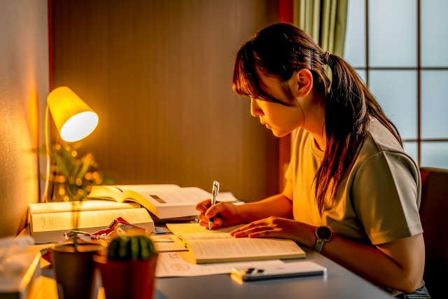 夜間 ライトをつけて机で勉強する女性
