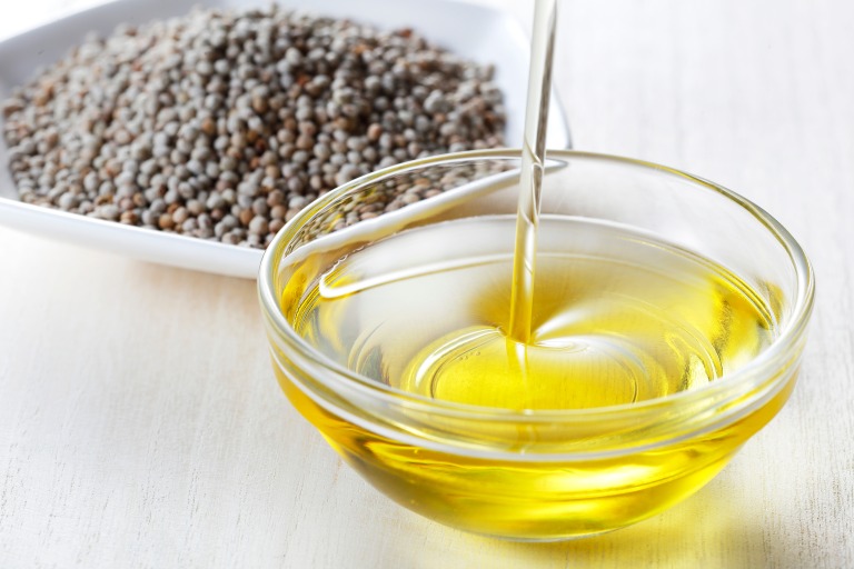 えごまの実を背景に木製スプーンでえごま油をガラス容器に注ぐ様子