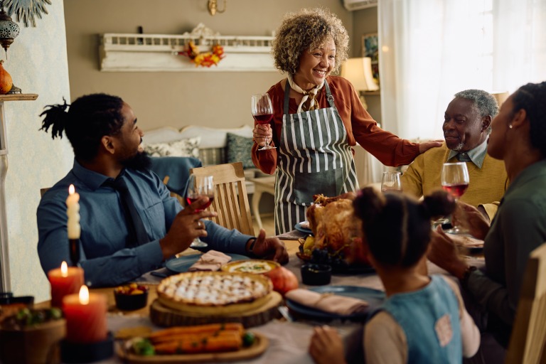 Happy multiracial extended family toasting during Thanksgiving meal at dining table. ダイニングテーブルで感謝祭の食事を囲み、乾杯する多民族の大家族