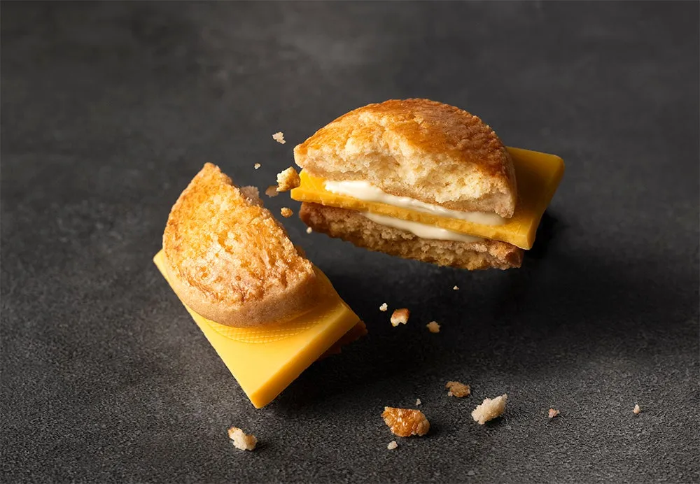 チーズサンドイッチが半分に割れた様子を捉えた写真。パン、チーズ、白いクリームのようなものが層になっており、背景は暗い色調。