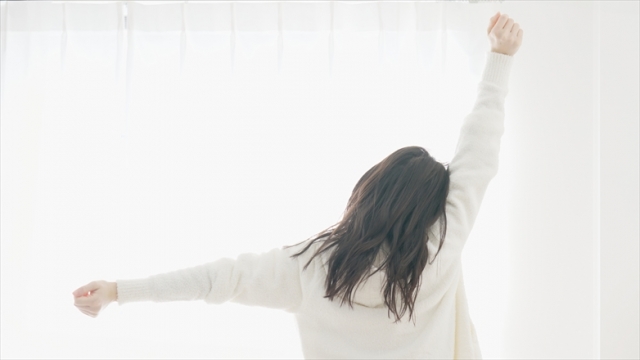 朝　起床イメージ　朝日に向かって伸びをする女性