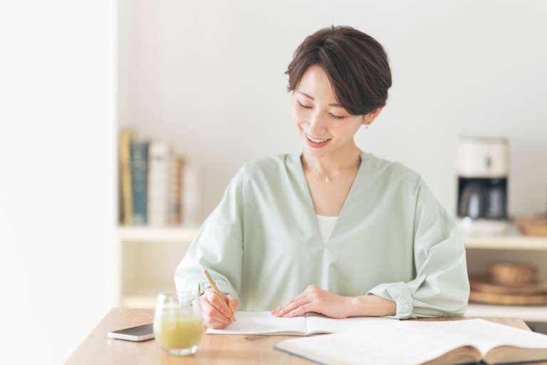 机でテキストを開き、ノートに書いている女性