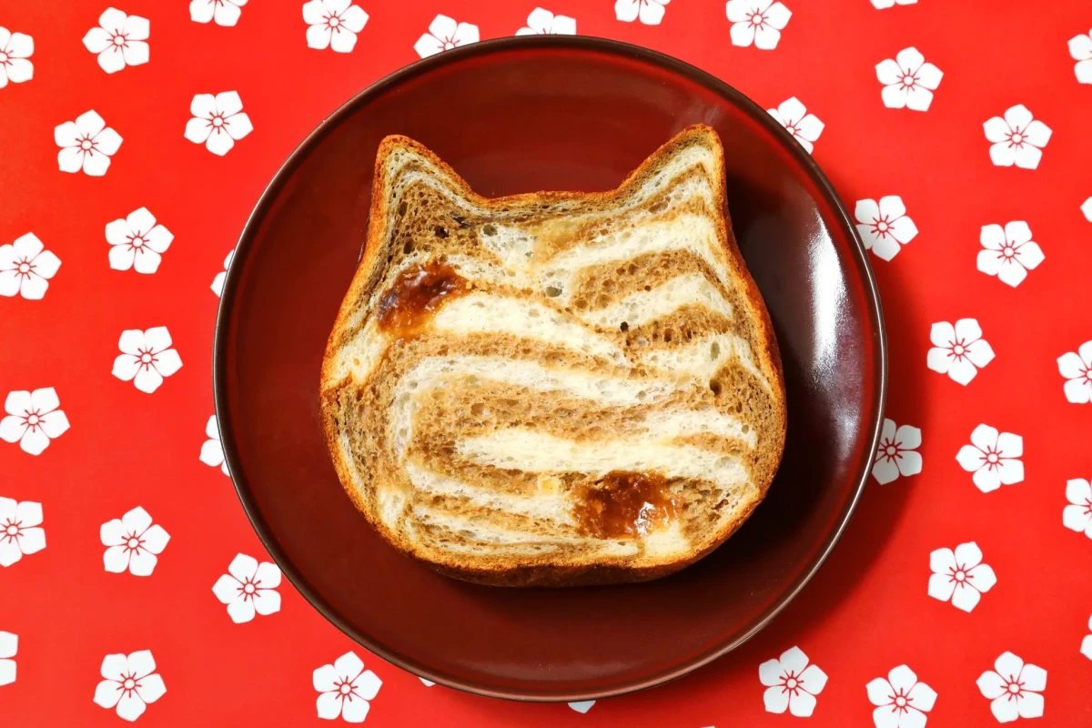 猫の形をしたトーストが皿の上に置かれており、背景は赤い花柄のデザインになっています。