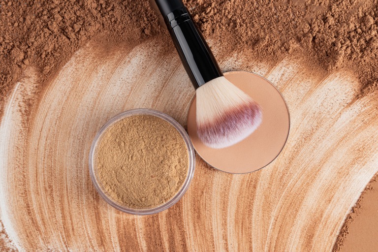 ナチュラルトーンのコンパクトパウダーとルースパウダーのジャーを、ダークトーンのドライパウダーのテクスチャーの上に重ねて塗布する。メイクブラシ。上からの眺め。