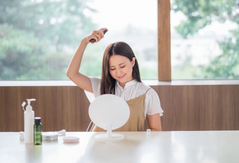 頭に日焼け止めスプレーをかける女性　イメージ