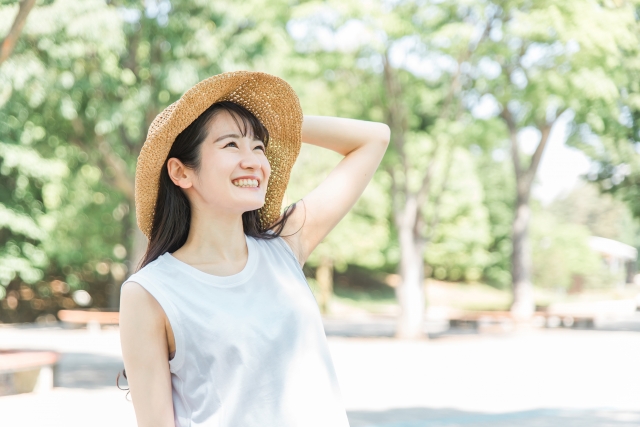 麦わら帽子をかぶって空を見上げるタンクトップの女性