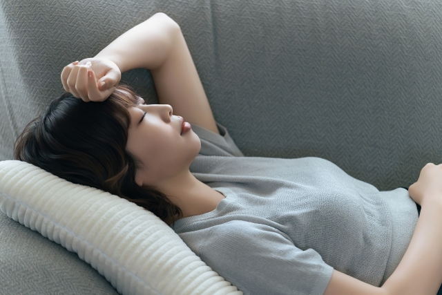 頭に手を当ててソファに寝込む女性