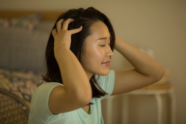 頭皮をマッサージする若い女性　夜に自室で
