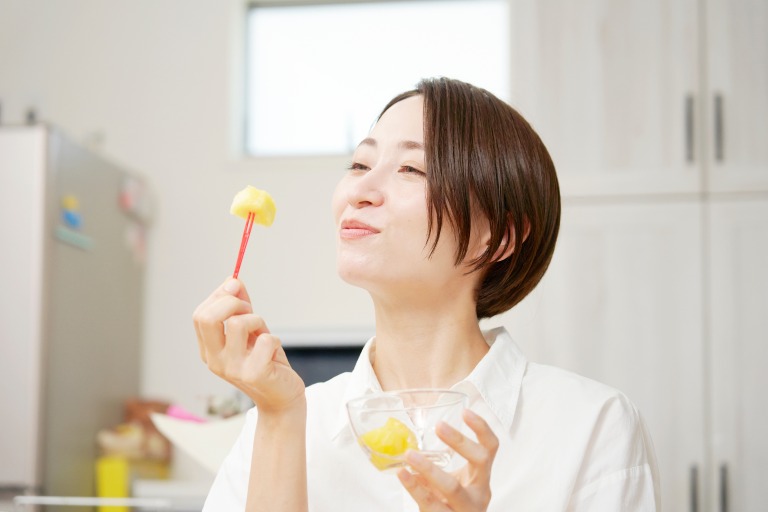 ダイニングでカットパインを食べる女性