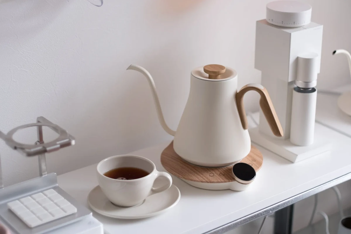 白い壁の前に置かれた、コーヒーポット、コーヒーミル、カップとソーサーに入ったお茶の静物写真。