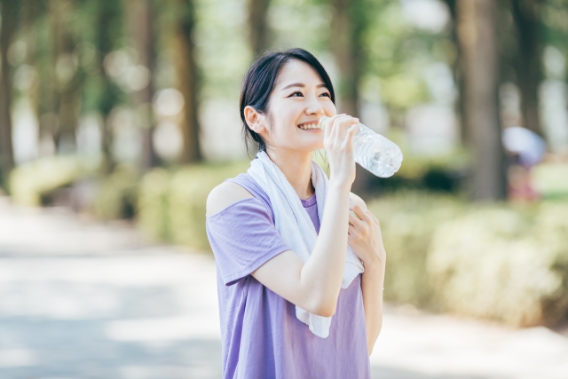 外で運動して水を飲む首にタオルをかけた女性