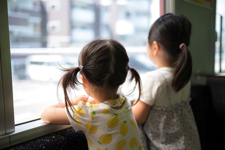 電車の車窓から外の景色を見て楽しむ女の子の姉妹