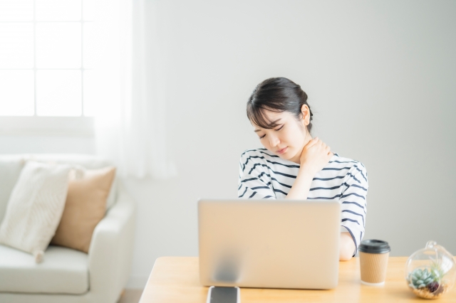 在宅イメージ　PCを開いて肩に手を当てる女性　肩こりイメージ