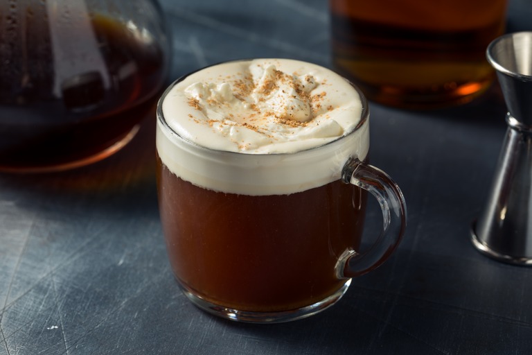 ガラスマグに入ったアイリッシュコーヒー　背景にガラスポットに入ったコーヒーとウイスキーが映る