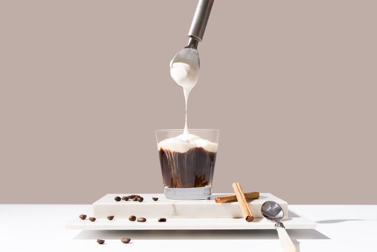 コーヒーに生クリームを乗せる様子　シナモンとコーヒー豆が散らばる
